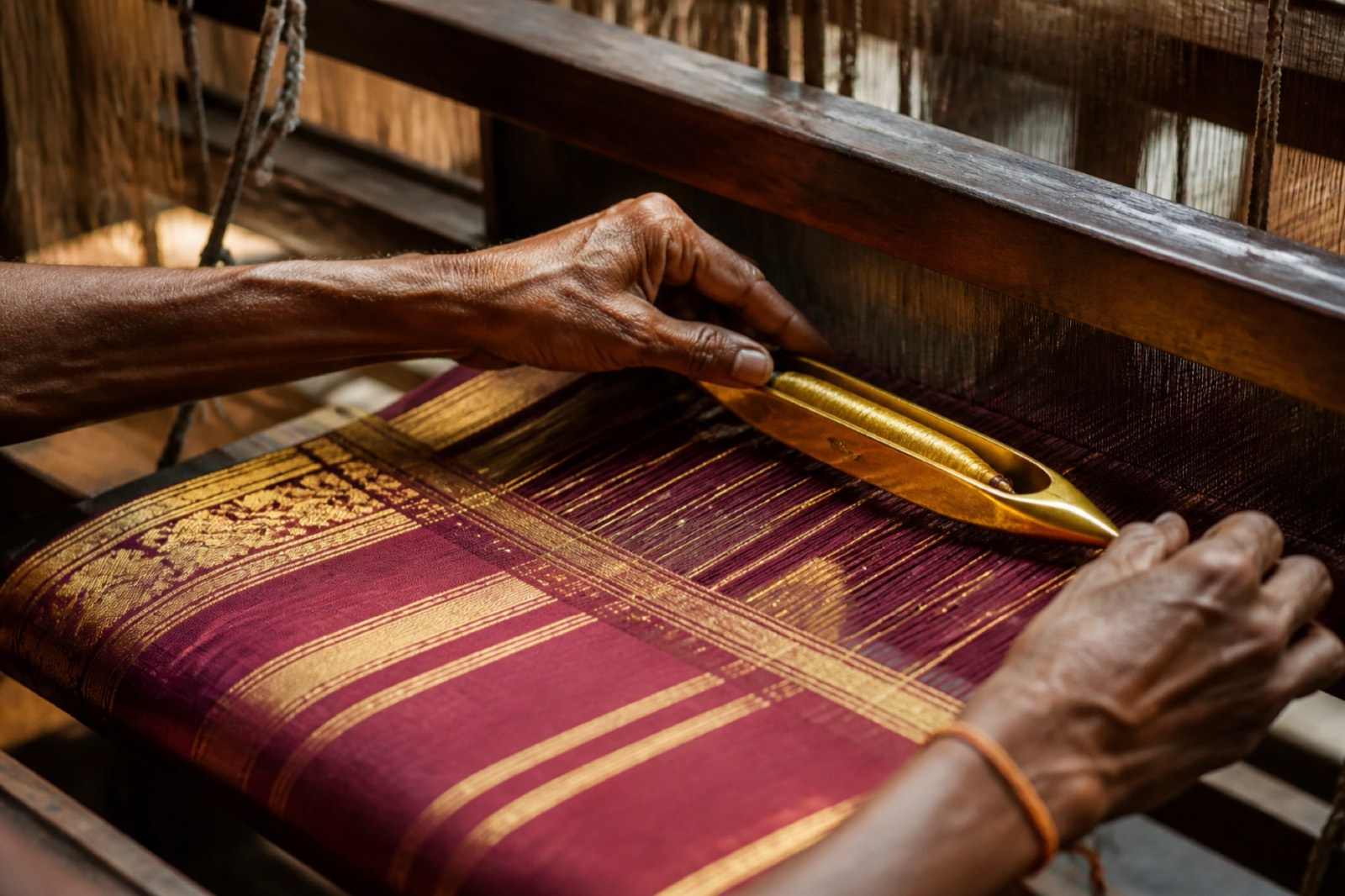 Hands weaving gold silk on a pit loom